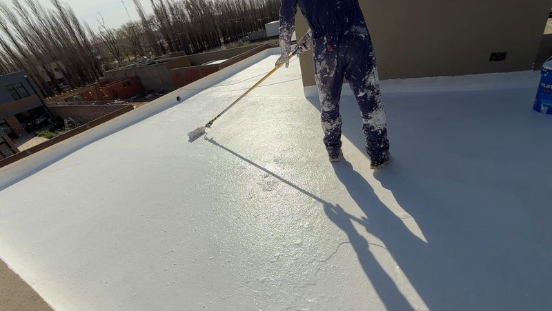 Operario de Sur Aislaciones aplicando membrana líquida blanca con rodillo sobre una terraza